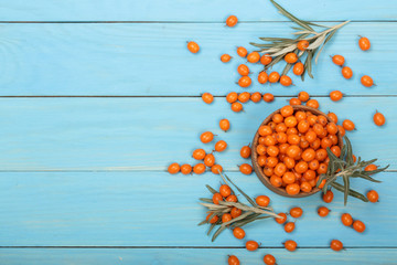 Sea buckthorn. Ripe fresh berries in bowl on blue wooden background with copy space for your text....