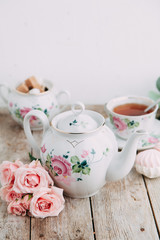tea set in composition with flowers and marshmallows. Coffee mug on a saucer, a teapot and a sugar...