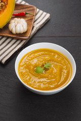 Pumpkin soup in a bowl with fresh pumpkins, garlic and parsley herbs