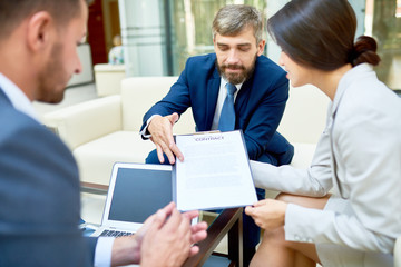 Confident business partners gathered together at boardroom and discussing details of mutually beneficial cooperation before signing contract