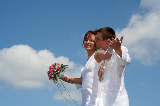 the groom holds the bride's hand against the blue sky