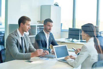 Confident business partners gathered together at modern boardroom and discussing details of their mutually beneficial cooperation, view through glass wall