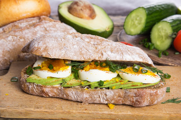 Avocado and egg sandwich on a wooden background. Fresh organic vegetables, eggs and whole wheat bread. Healthy breakfast. Rustic style.