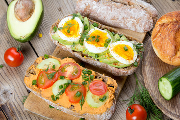 Sandwiches with avocado, eggs and tomato on a wooden background. Fresh organic vegetables, eggs and whole wheat bread. Healthy breakfast. Retro style.