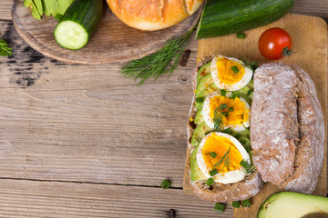 Avocado and egg sandwich on a wooden background. Fresh organic vegetables, eggs and whole wheat bread. Healthy breakfast. Rustic style.