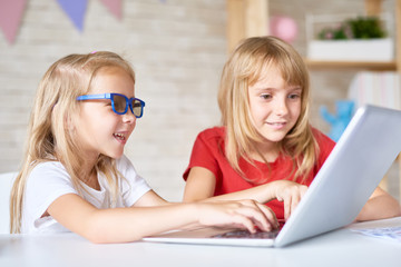 Portrait of two little girls using laptop together while playing at home in cozy playroom