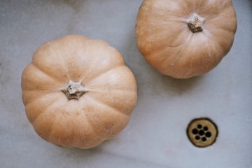 Top close up view of two fresh raw orange pumpkins laying in white beautiful marble sink prepared for cooking.