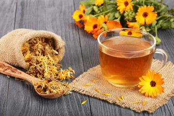 Calendula tea with fresh and dried flowers on black wooden background