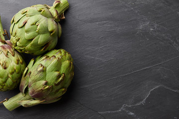 Fresh ripe artichokes close up on textured stone background, top view