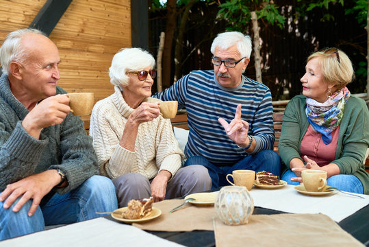 Senior friends wearing knitted sweaters chatting animatedly with each other while having tea party at lovely patio