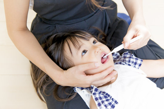 母に歯を磨いてもらう幼い女の子