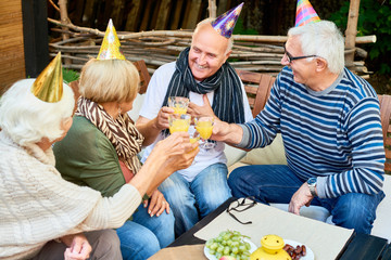 Portrait of smiling senior man wearing party hat toasting with group of friends while celebrating his birthday at outdoor cafe