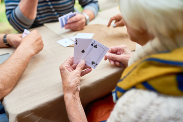 Close-up shot of unrecognizable senior woman playing poker with friends while sitting at outdoor cafe table, over shoulder view