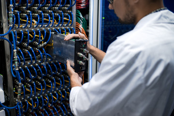 Back view portrait of unrecognizable man in lab coat taking out blade server while working with...