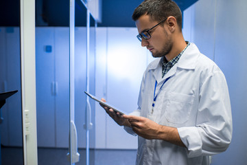 Side view portrait of young network engineer looking at digital tablet while standing between...