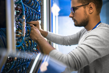 Young man connecting cables in server room