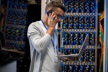 Side view  portrait of young man speaking by phone and using laptop against background of blade...