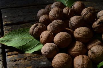 a pile of walnuts and green leaves of walnut on a dark wooden table