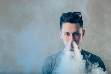 Men with beard in sunglasses vaping and releases a cloud of vapor in nose