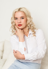 Beautiful young blonde woman in a white blouse sitting on a sofa