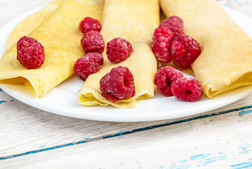 Rolled pancakes with raspberry on the plate.