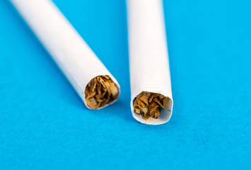 Two cigarettes on a blue background. Close up.