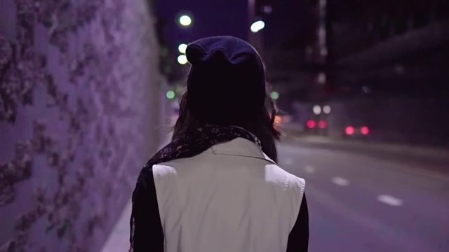 Teenage girl walking along night city street and turns her head to the camera, slow motion