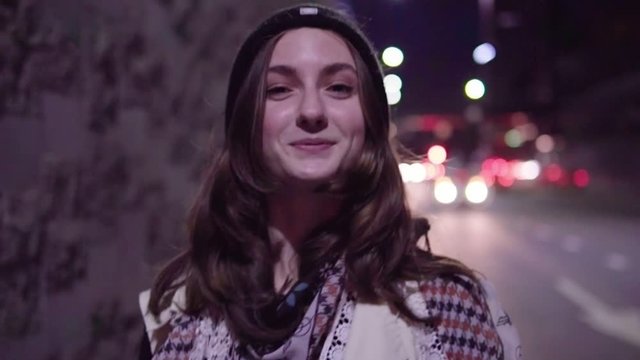 Close-up of a happy teenage girl walking along night city street, slow motion