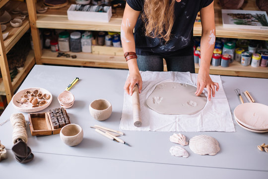 female potter molding clay with rolling pin in pottery workshop