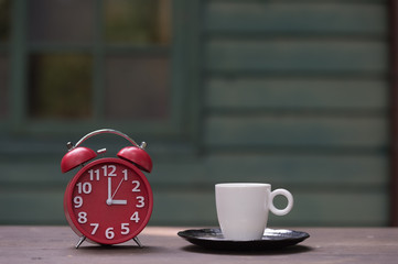 Retro alarm clock with five minutes to twelve o'clock.coffee cup on wooden table .