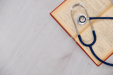 Beautiful stethoscope lying on a reference books. Stethoscope with open book on wooden background. Medical literature concept. copy space for text, selective focus Top view - obrazy, fototapety, plakaty