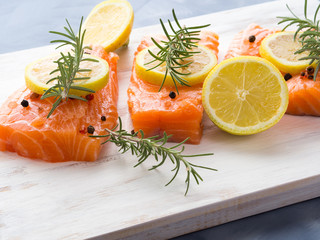 Raw salmon pieces on wooden board with herbs, salt and spices