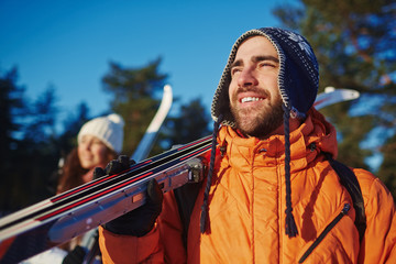 Smiling man with skis and his wife looking at something curious during trip in winter forest