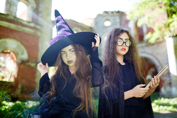 Two spooky girls in witch costumes on background of ruined castle