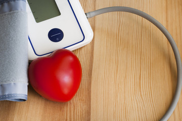 A blood pressure cuff and a red heart on a wooden table.