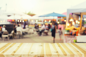 Blurred image of food fairs and food festivals consist of many booth and vendors at food stalls. People walking in street. Event in Chiang Mai at twilight montage with wood table top for background.