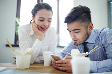 Mobile professionals watching curious video in smartphone during lunch break