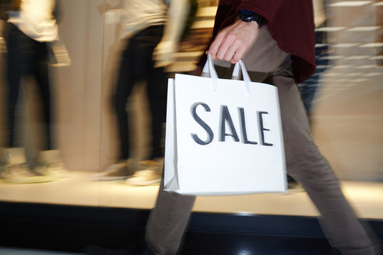 Hurrying guy with shopping bag moving slong window display in the mall during seasonal sale