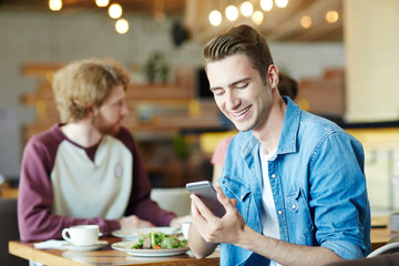 Modern guy in denim shirt reading hot offer in his smartphone while sitting in cafe