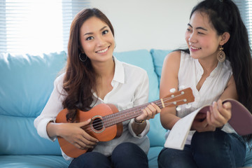 Two asia women are having fun playing ukulele and smiling at home for relax time