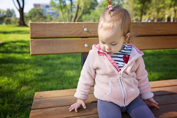 Eighteen months old toddler girl climbing on the wooden bench in the park on a sunny autumn day