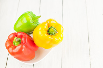 Red yellow and green fresh whole raw pepper in ceramic bowl on old white rustic planks