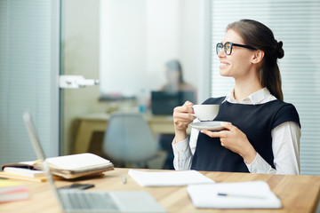 Young female with cup of tea having break by her workplace in office