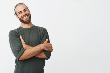 Fototapeta Attractive swedish man with stylish hair and beard laughs at funny story from friend with crossed hands and closed eyes. obraz