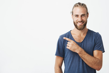 Happy beautiful bearded guy with good-looking hairstyle looking at camera, smiling and pointing...