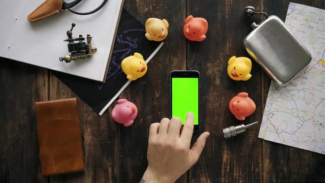Adorable and funny top view video of wooden table arranged with travel perks and essentials, business smartphone lays in middle of group of cute random rubber ducks toys, swipe color chroma key screen