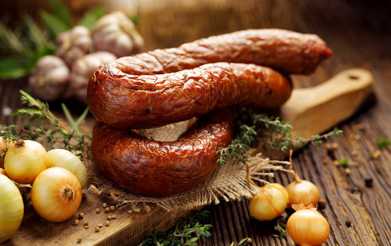 Smoked Polish sausage on a wooden rustic table with addition of fresh aromatic herbs and spices, natural product from organic farm, produced by traditional methods
