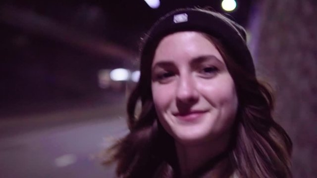 Close-up of a happy teenage girl walking along night city street, slow motion