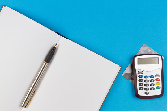 Electronic password generator for internet banking, payment card and open paper notebook with pen on blue background