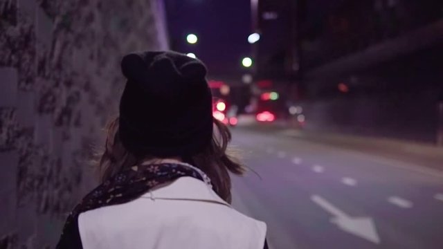 Woman walking along night city street, slow motion